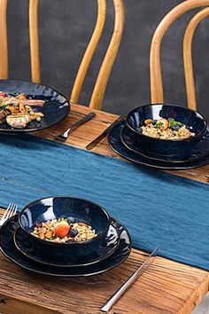 four black plates with food on them sitting on a table in front of some chairs