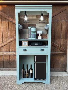 a blue cabinet with two bottles on it and some lights hanging from the top, in front of a barn door