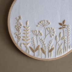 a white embroidered wall hanging with flowers and leaves on it's side, in front of a beige wall