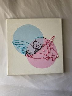 a small square painting with an angel on it's back and pink, blue, and white background