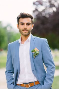 a man in a blue suit with a flower on his lapel is posing for the camera