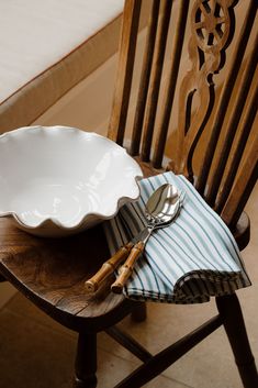 a wooden chair with a white bowl and silverware on it next to a blue striped napkin