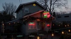 the outside of a restaurant at night with lights strung from it's windows and tables