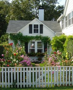 a white picket fence in front of a house with flowers growing on the side of it