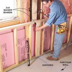 a man in blue shirt and jeans working on wall framing with tools next to it