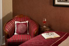 a red chair sitting next to a bed with a book and wine glass on top of it