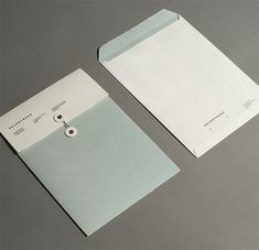 two white envelopes are sitting next to each other on a gray surface, one is open and the other has a button