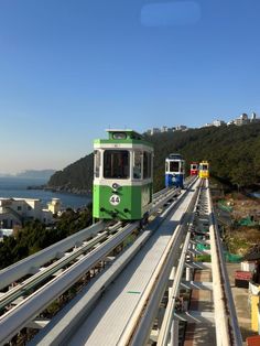 two green and white trains traveling down tracks next to each other on a bridge over looking the ocean