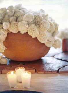 some candles are sitting on a table with flowers in a bowl and two smaller ones