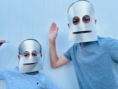 two children wearing paper masks with their hands in the air and one holding up his hand