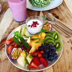 a plate full of fruit and yogurt on a wooden table with silverware