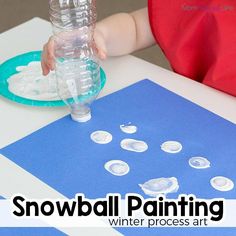 a baby is playing with snowball painting on the table next to a water bottle