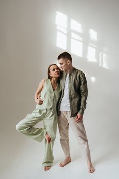 a man and woman are posing for a photo in front of a white wall with sunlight coming through the window