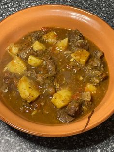 a brown bowl filled with meat and potatoes on top of a granite counter next to a knife