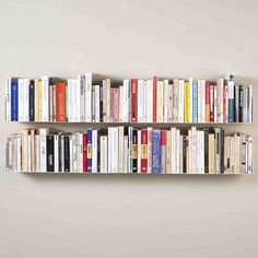 a book shelf filled with lots of books on top of a white wall next to a gray wall