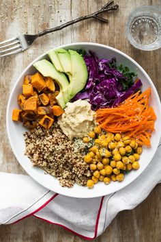 a white plate topped with lots of food on top of a wooden table next to a fork