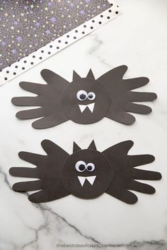 two black paper cut outs with googly eyes and mouth shapes on a marble surface