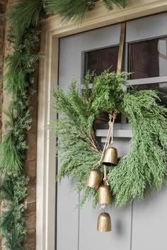 a christmas wreath with bells hanging from it's side and evergreen branches on the front door