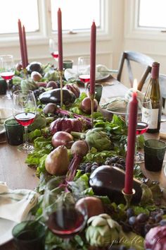 the table is set with many different types of vegetables and wine glasses on it, along with candles