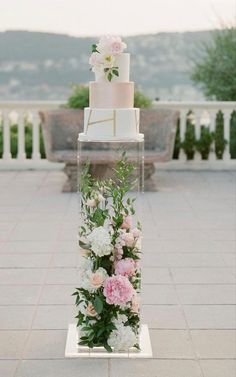 a wedding cake with pink and white flowers on display in front of an outdoor setting