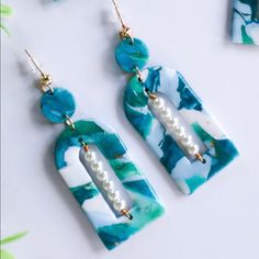 two pieces of jewelry with pearls hanging from them on a white table next to flowers