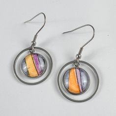 Round watercolor earrings featuring vertical orange, purple and blue stripes. A delicate circular metal frame surrounds the main part of the drop earrings. Artistic Multicolor Hypoallergenic Jewelry, Retro Circle Jewelry Gift, Multicolor Hand Painted Metal Jewelry, Hand Painted Multicolor Metal Jewelry, Nickel-free Glass Drop Jewelry, Modern Hand Painted Multicolor Jewelry, Multicolor Round Retro Jewelry, Multicolor Nickel-free Retro Jewelry, Retro Multicolor Round Jewelry