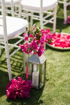 pink flowers and candles are on the grass near white chairs with flower petals in them