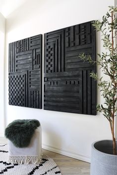 two black art pieces hanging on the wall next to a potted plant and rug