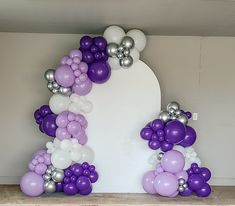 purple and white balloons are arranged in the shape of an arch for a balloon display