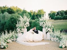 a bride and groom are sitting on a bench surrounded by white flowers, greenery and candles