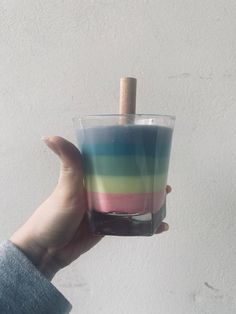 a person holding up a glass with colored liquid in it and a wooden stick sticking out of the top