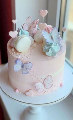 a pink cake with butterflies and hearts on top is sitting in front of a window