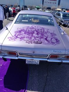 a car that has been painted with some pictures on the front and back side, sitting in a parking lot next to other cars