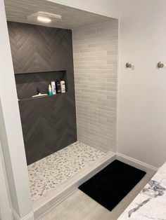 a bathroom with white and gray tile walls, black rugs and a shower stall