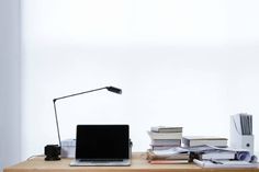 a laptop computer sitting on top of a wooden desk next to stacks of books and papers