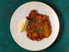 a white plate topped with fried chicken next to a lemon wedge on a green table