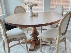 a round table with four chairs around it in front of a window and rug on the floor