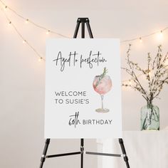 a welcome sign for someone's 60th birthday with a cocktail glass on it and lights in the background