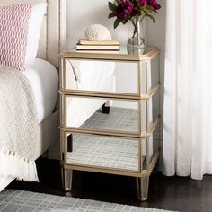 a nightstand with flowers on top of it next to a white bedspread and pillows