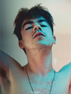 a shirtless young man with his eyes closed wearing a necklace that has a cross on it