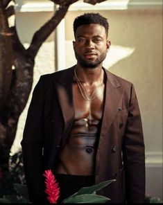 a man standing in front of a tree wearing a brown jacket and black pants with no shirt on