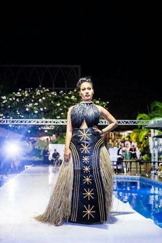 a woman is standing in front of a pool at night wearing a dress with feathers on it