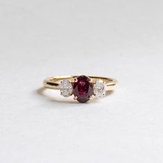 a three stone ring with two diamonds on the side and a red ruby in the middle