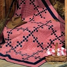 a pink quilt and hat sitting on top of a wooden bench next to a fence