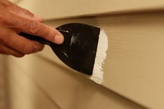 a person with a brush painting the side of a house's exterior sidings