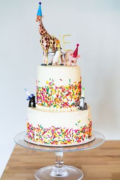 a three tiered cake with sprinkles and animals on top sits on a wooden table