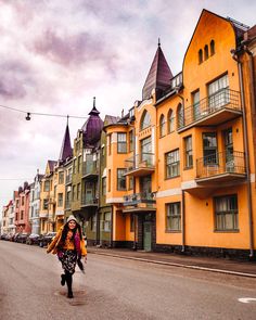 a woman is walking down the street in front of some yellow buildings on a cloudy day