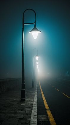 a street light sitting on the side of a road next to a lamp post in the fog