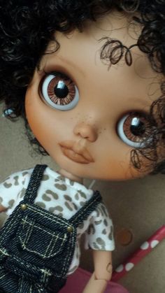 a close up of a doll with curly hair and blue eyes, wearing overalls