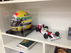 a yellow race car in a clear case on a book shelf next to a magazine